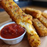 Close-up of golden, crispy Air Fryer Mozzarella Sticks with melted cheese pull and marinara dipping sauce.