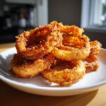 A stack of golden brown, crispy Air Fryer Onion Rings on a white plate, ready to eat.