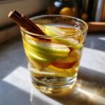 Glass of apple cinnamon flavored water with apple slices and cinnamon sticks.