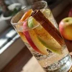 Glass of apple cinnamon flavored water with apple slices and a cinnamon stick.