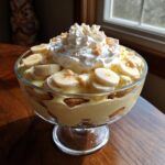 A beautiful glass bowl filled with Banana Pudding Trifle, topped with whipped cream, banana slices, and cookie crumbles.