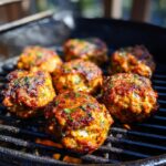 Close-up of BBQ Chicken Meatballs grilling on a charcoal grill, topped with herbs.