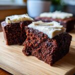 Close-up of frosted Carrot Brownies on a wooden board. The brownies have a rich, dark color and creamy white frosting.