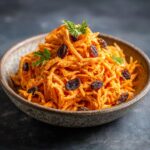 Close-up of a bowl of Carrot Raisin Salad, garnished with fresh herbs and plump raisins.