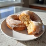 Two glazed Carrot Spice Donuts on a white plate, one donut is halved to show the inside texture.
