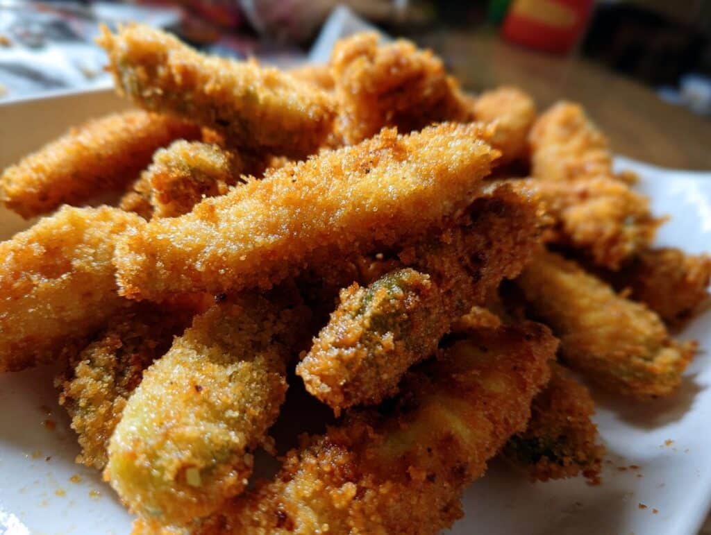 A pile of crispy, golden-brown cheese-wrapped pickles on a white plate, ready to be enjoyed.