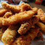 A pile of crispy, golden-brown cheese-wrapped pickles on a white plate, ready to be enjoyed.