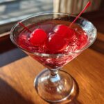 A vibrant cherry martini in a stemmed glass, garnished with three bright red maraschino cherries.