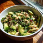 A bowl of fresh Chicken Avocado Salad with avocado slices, chicken, herbs, and red onion.