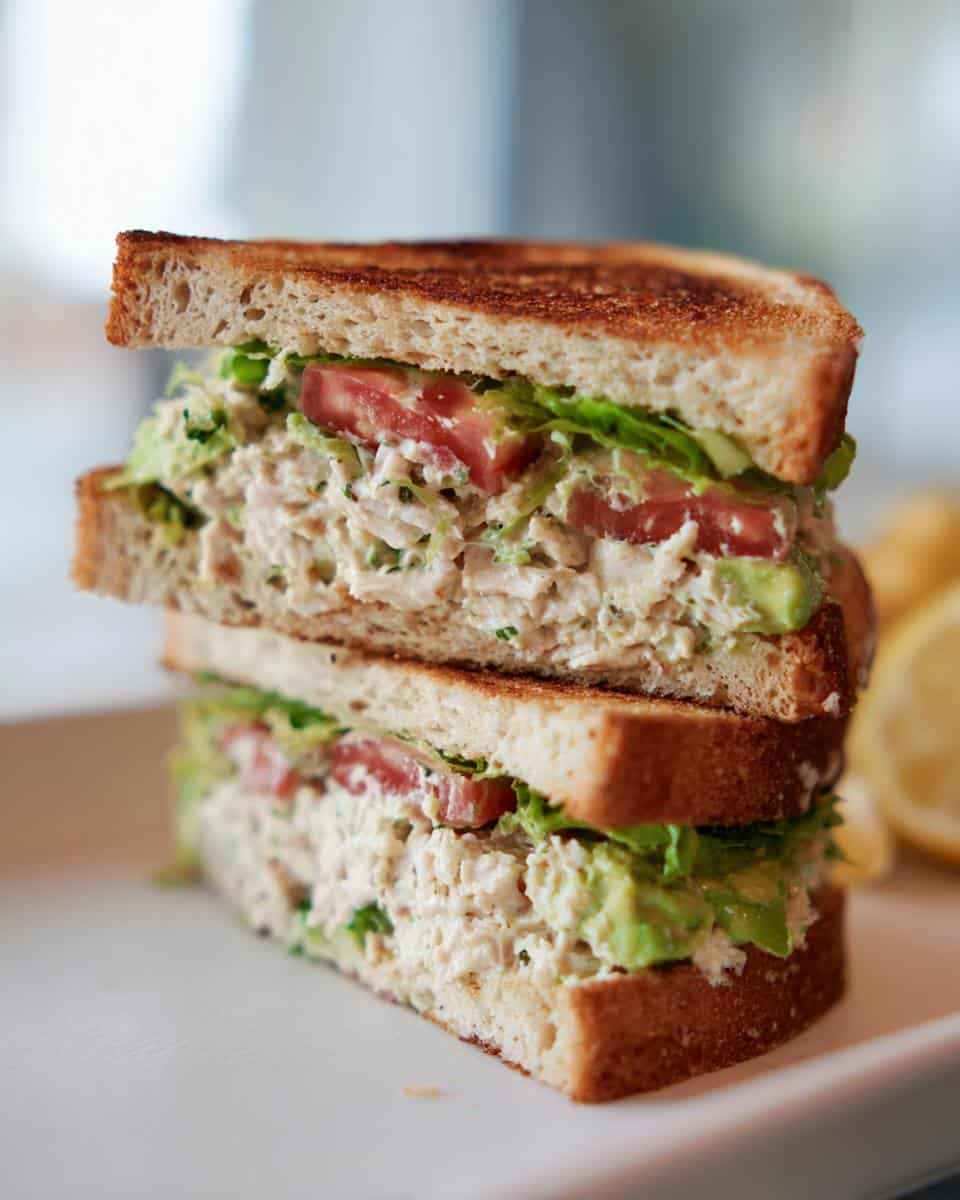Stacked Creamy Chicken Avocado Sandwich with toasted bread, chicken salad, avocado, tomato, and lettuce.
