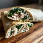 Two halves of a Chicken Spinach Wrap stacked on a wooden board, showcasing the chicken, spinach, and creamy filling.