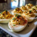 A close-up of Classic Deviled Eggs garnished with paprika and fresh chives on a white platter.