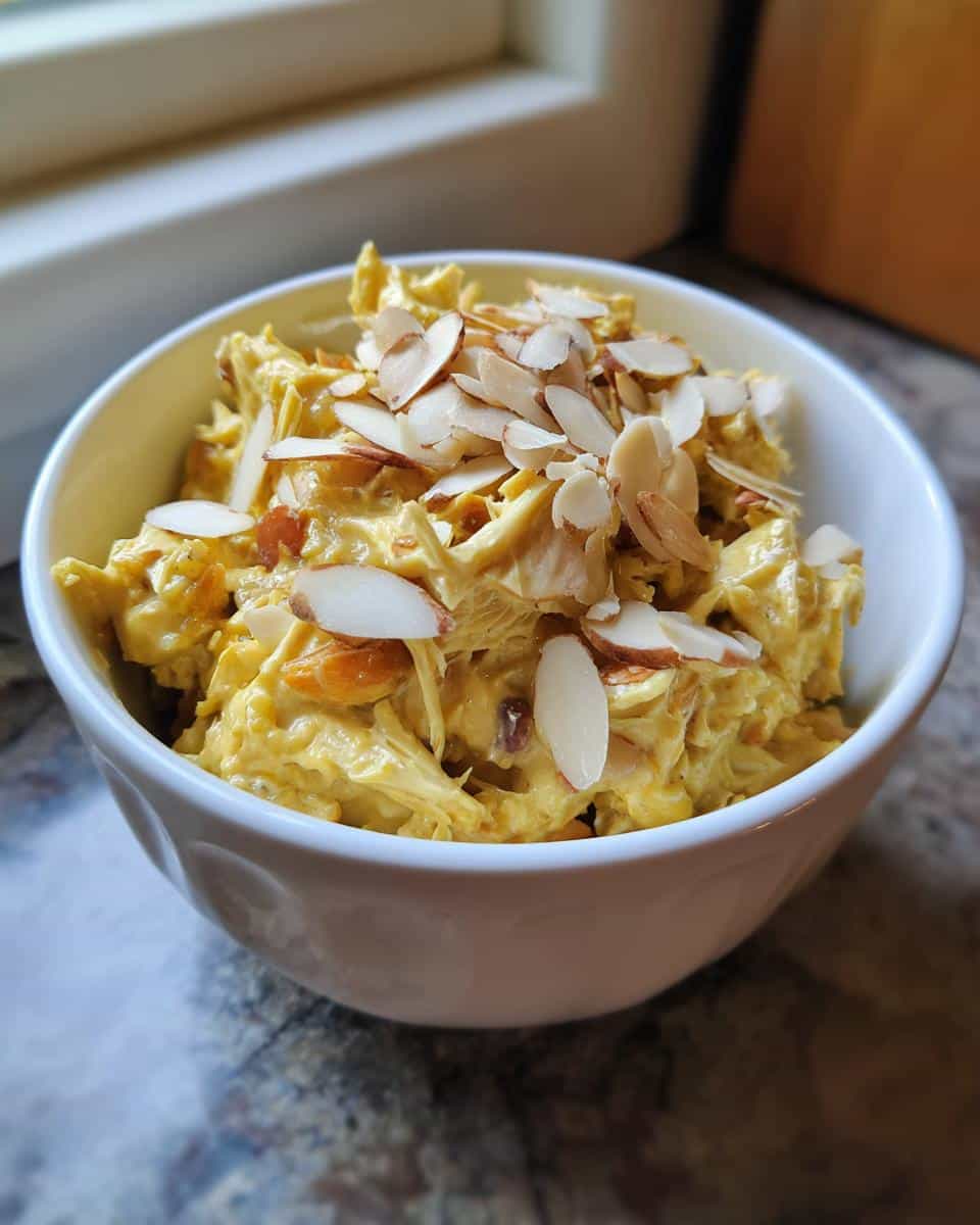A bowl of creamy Coronation chicken salad topped with toasted almond slices.