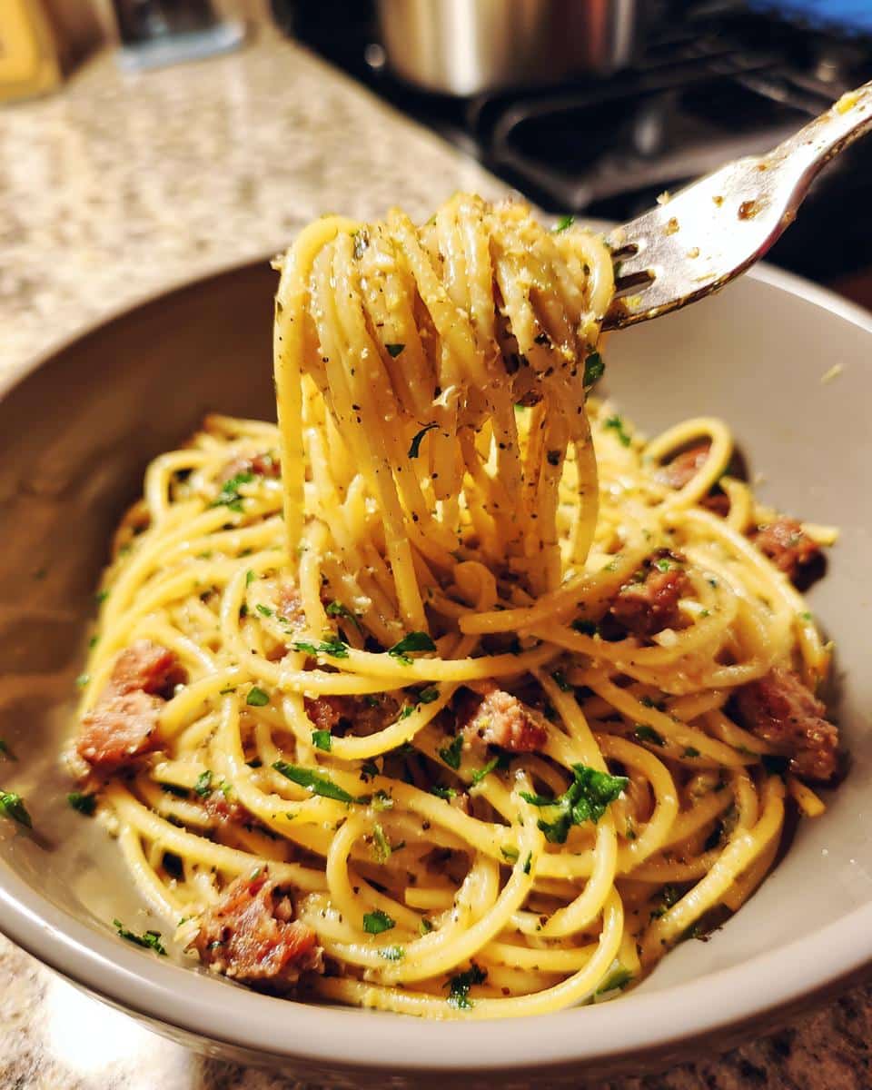 A fork lifts a swirl of spaghetti coated in creamy sauce, mixed with pieces of smoked sausage and fresh parsley. Creamy Smoked Sausage Pasta.