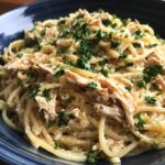 A close-up of Crockpot Garlic Parmesan Chicken Pasta, featuring spaghetti noodles coated in creamy sauce, shredded chicken, and fresh parsley.