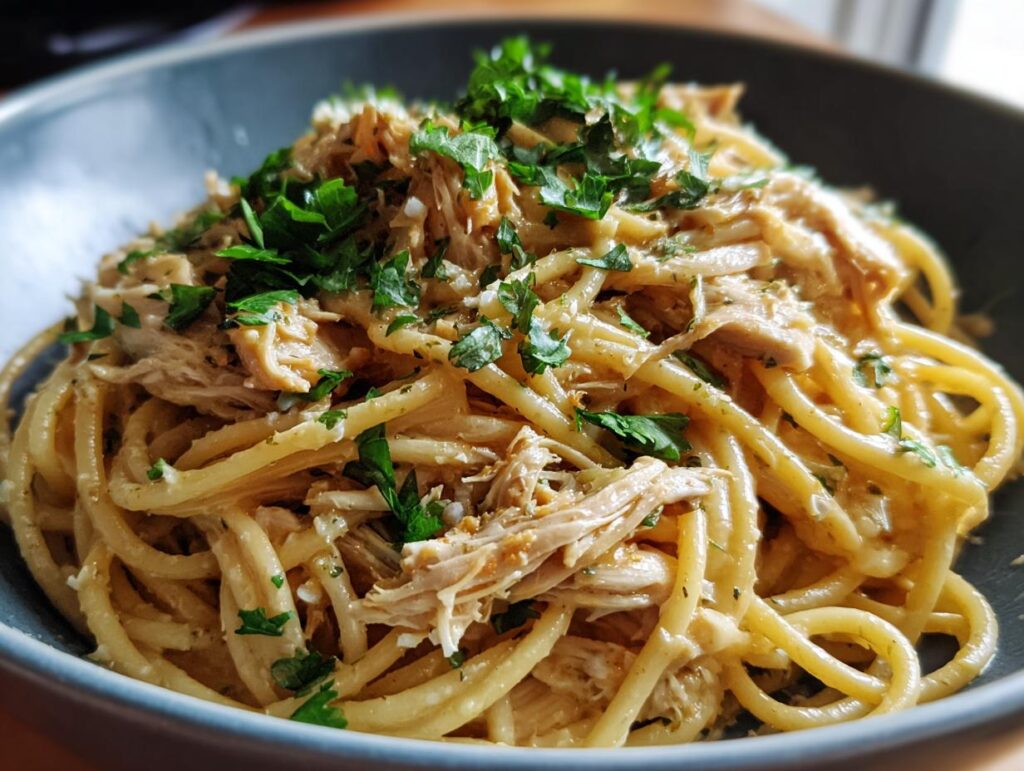A close-up of Crockpot Garlic Parmesan Chicken Pasta, featuring spaghetti noodles coated in creamy sauce with shredded chicken and fresh parsley.