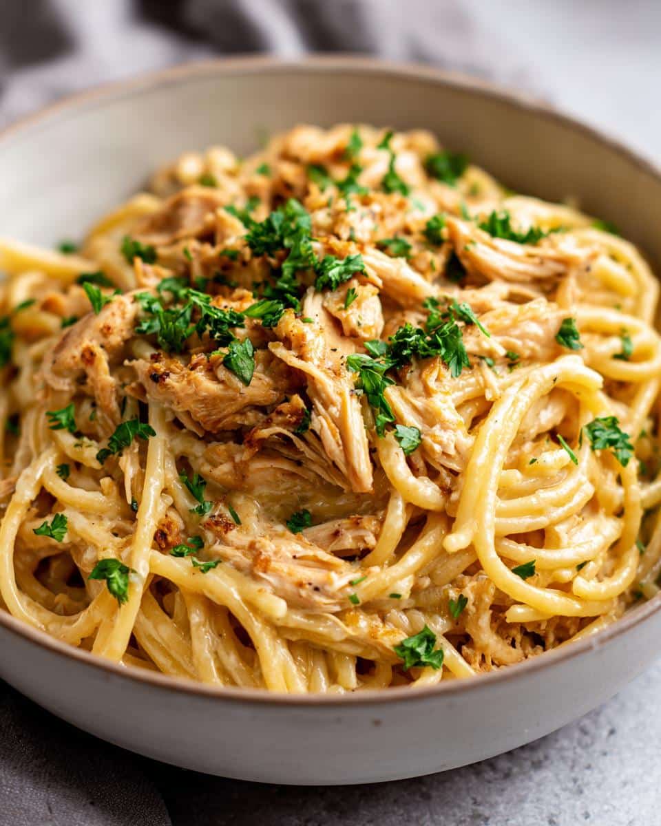 A close-up of a bowl filled with Crockpot Garlic Parmesan Chicken Pasta, topped with fresh parsley.