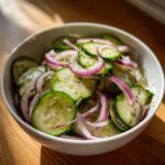 Bowl of Cucumber salad with sliced cucumbers, red onion, and herbs.
