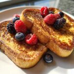 Two slices of custard yogurt toast topped with raspberries, blueberries, and blackberries.
