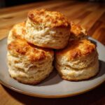 A stack of golden-brown, fluffy homemade biscuits on a grey plate, showcasing their flaky layers.
