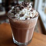 A tall glass of frozen hot chocolate topped with whipped cream and chocolate shavings.