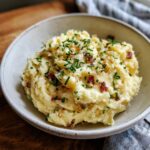 A close-up of creamy Garlic Mashed Potatoes generously topped with fresh chives and crispy bits.