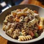 A close-up of a bowl filled with creamy tuna pasta salad, featuring rotini pasta, tuna chunks, carrots, and celery.