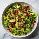 Overhead shot of a Green goddess salad in a white bowl, featuring lettuce, avocado, and a savory topping.