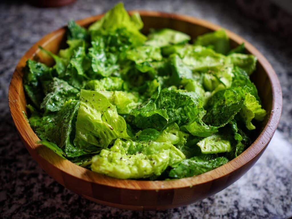 A wooden bowl filled with fresh green goddess salad, featuring crisp lettuce and a creamy dressing.