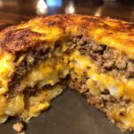 Close-up of a slice of hamburger potato casserole, showing layers of ground beef and melted cheese over potatoes.