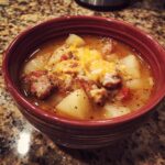 A close-up of a bowl of hearty sausage potato soup, topped with melted cheddar cheese.