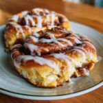 Close-up of two fluffy homemade cinnamon rolls drizzled with white icing on a plate.