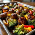 Close-up of Honey Garlic Sheet Pan Sausage with broccoli, bell peppers, and onions, glazed in a shiny sauce.