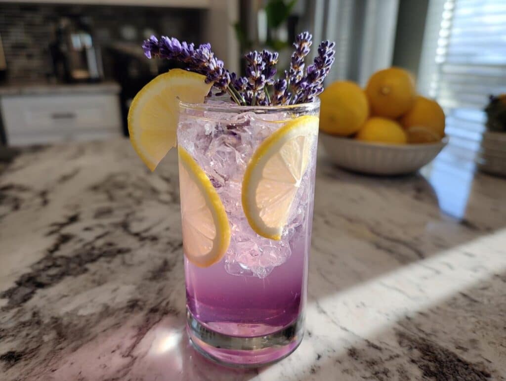 A tall glass of purple lavender lemonade filled with ice, garnished with lemon slices and fresh lavender sprigs.