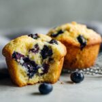 Close-up of Lemon Blueberry Muffins, one with a bite taken out, revealing blueberries.