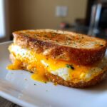 Close-up of a one-pan egg breakfast sandwich with a runny yolk and toasted bread.