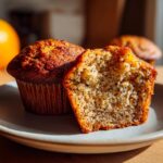 Close-up of a halved Orange Poppy Seed Muffin showing the texture, next to a whole muffin on a plate.