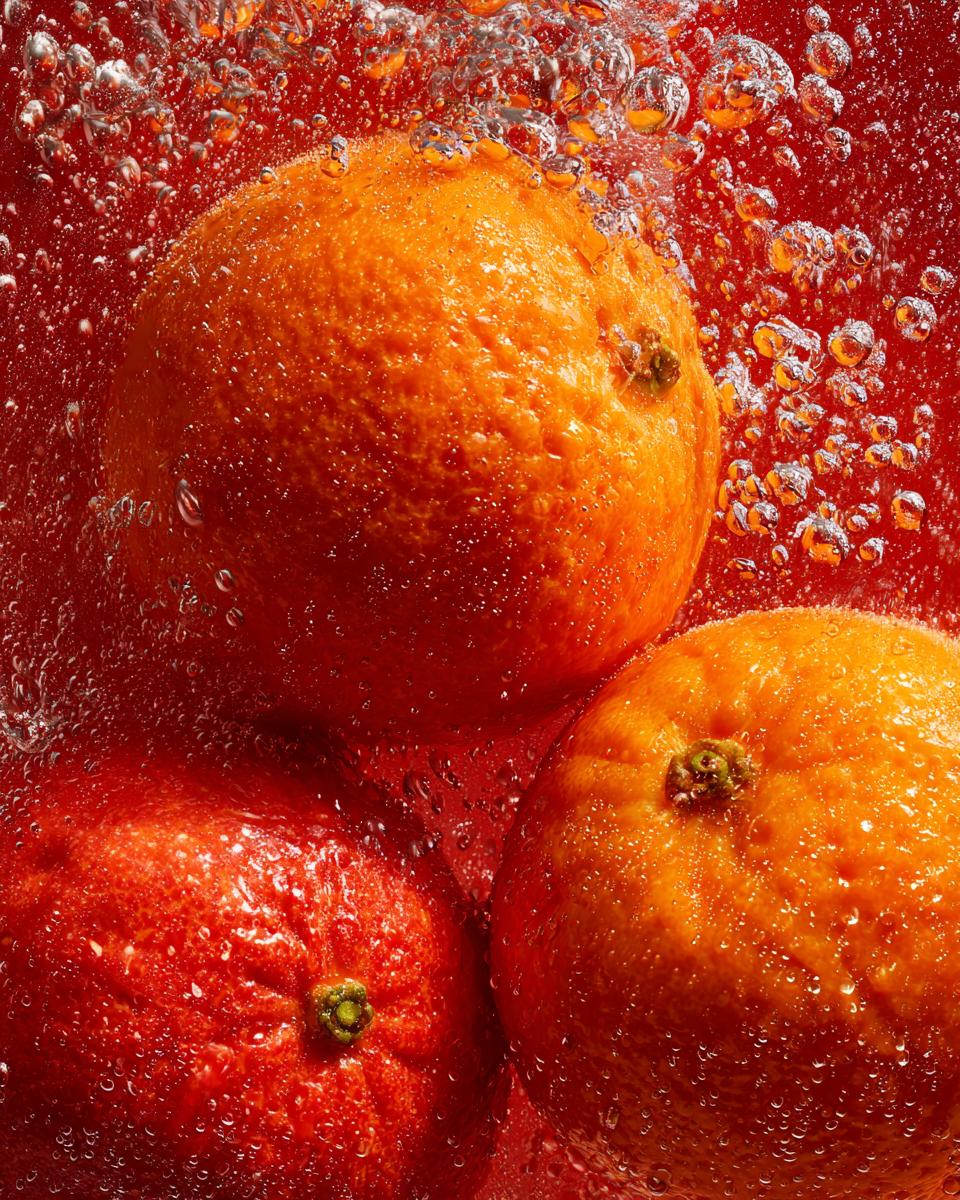 Three fresh oranges submerged in water, showing bubbles, for a Classic Orangeade recipe.