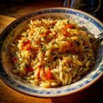 A colorful bowl of Orzo pasta salad with tomatoes and herbs, ready to be served.
