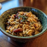 A bowl of delicious orzo pasta salad with sun-dried tomatoes and herbs, ready to eat.
