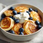 A bowl of pancake cereal topped with blueberries and whipped cream. Delicious breakfast treat!
