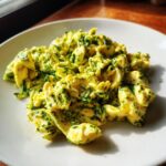 A plate of vibrant pesto-scrambled eggs, showcasing the bright green pesto mixed with the yellow eggs.