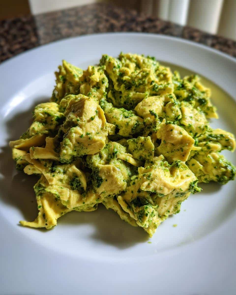 A serving of pesto-scrambled eggs on a white plate, showcasing the vibrant green pesto mixed with the yellow eggs.