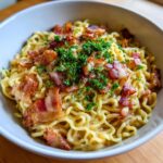Bowl of creamy Ramen carbonara topped with crispy bacon and fresh parsley.