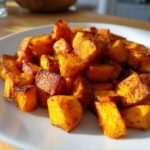 Close-up of perfectly roasted sweet potato recipe cubes on a white plate, showing caramelized edges.