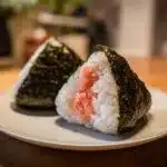 Two triangle-shaped onigiri rice balls, one with a salmon filling, wrapped in nori seaweed on a plate.