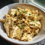 A bowl of tender shredded chicken breast, a key ingredient in delicious chicken breast crockpot recipes, garnished with parsley.