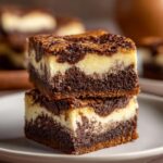 Two decadent slutty cheesecake bars stacked on a plate, showcasing layers of chocolate and cream cheese.