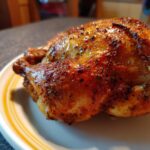 A perfectly cooked Spiced Roast Chicken sits on a plate, showcasing its golden-brown, crispy skin.