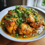 A delicious plate of Spicy Chicken Curry, garnished with fresh cilantro, parsley, and sliced green chilies.